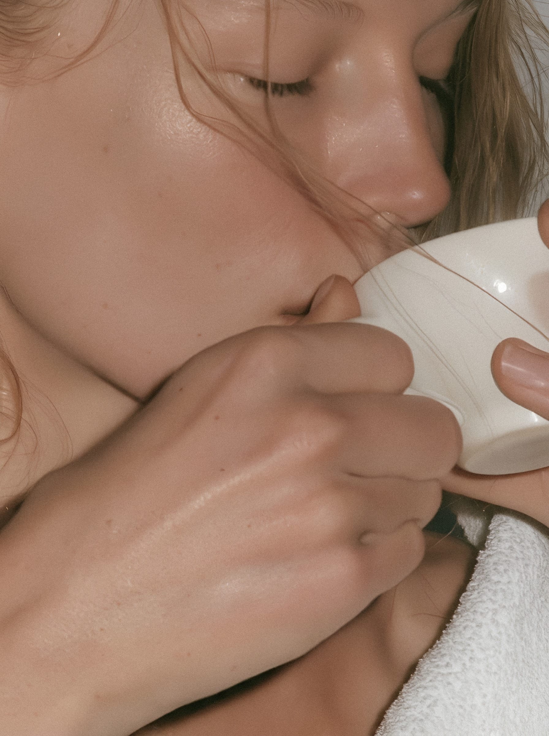 A woman with closed eyes holding a white cup in both hands.