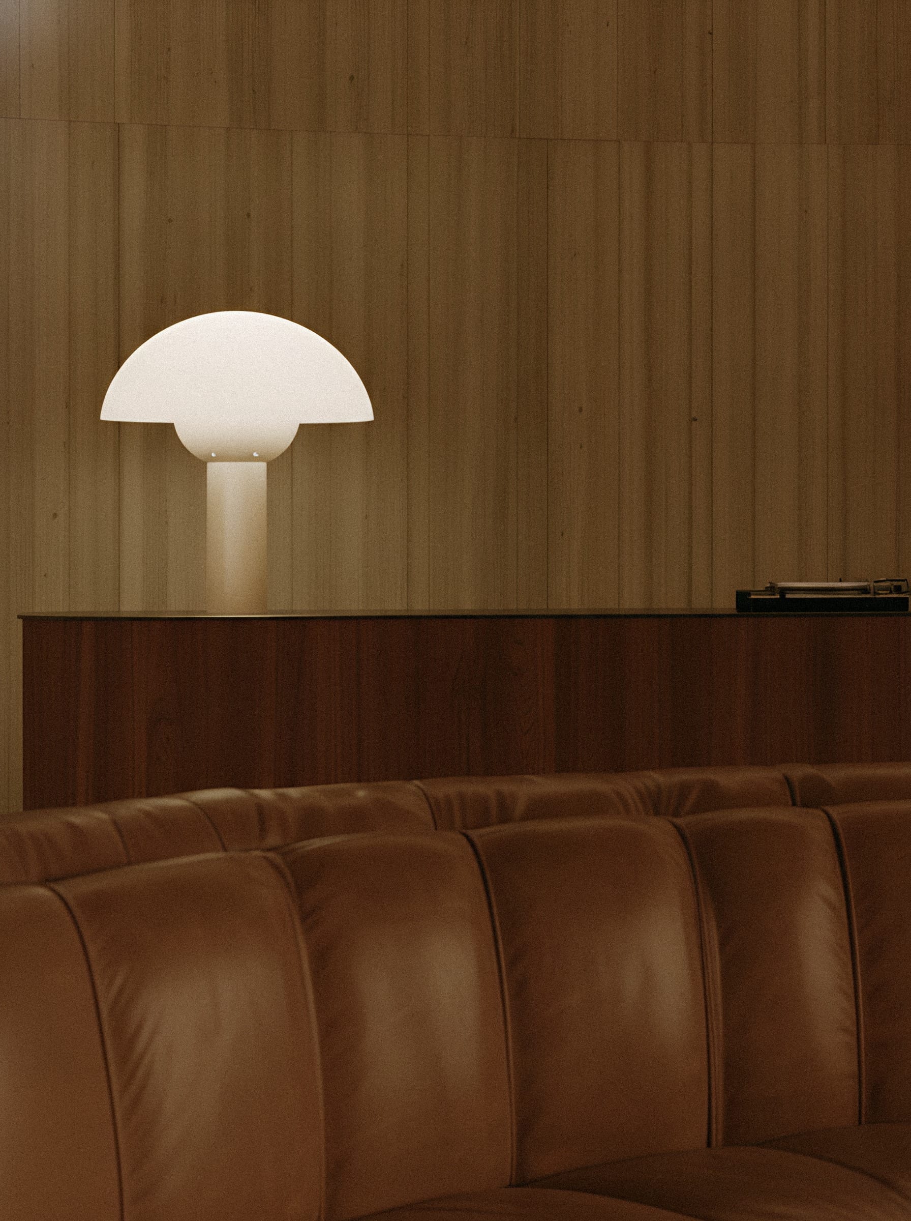 A white dome-shaped lamp above a brown leather sofa against wooden panelling.