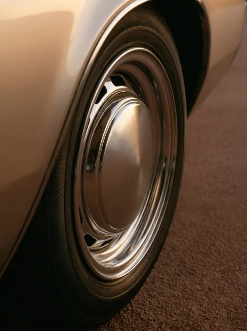A polished metal wheel and black tire beneath warm cream car bodywork.